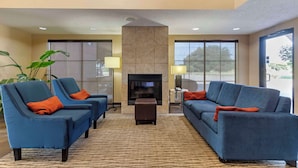 A modern hotel lobby with two blue sofas, a small ottoman, a fireplace, and large windows. - Comfort Inn & Suites Seguin (Seguin)