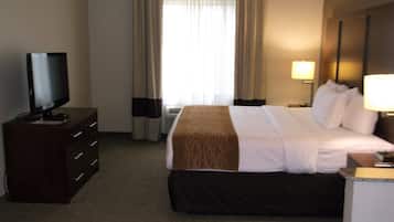 Una habitación de hotel con una cama, un televisor sobre una cómoda, una lámpara y una ventana con cortinas.