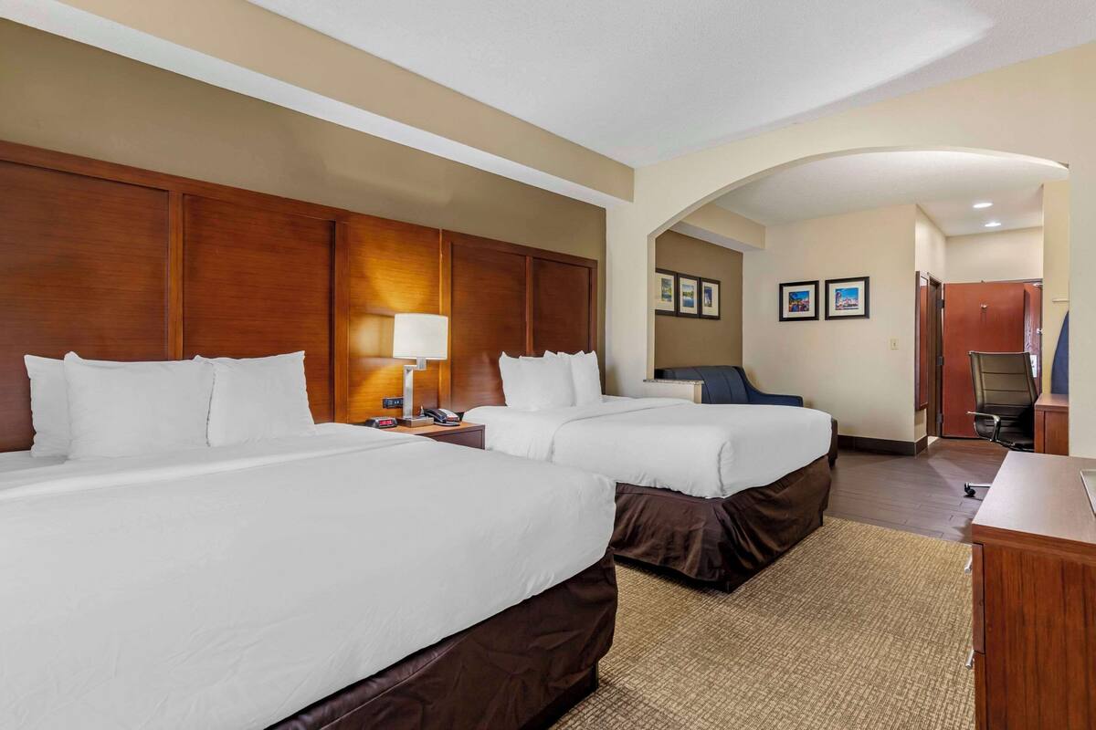 A hotel room with two beds, a desk, a chair, and a lamp.