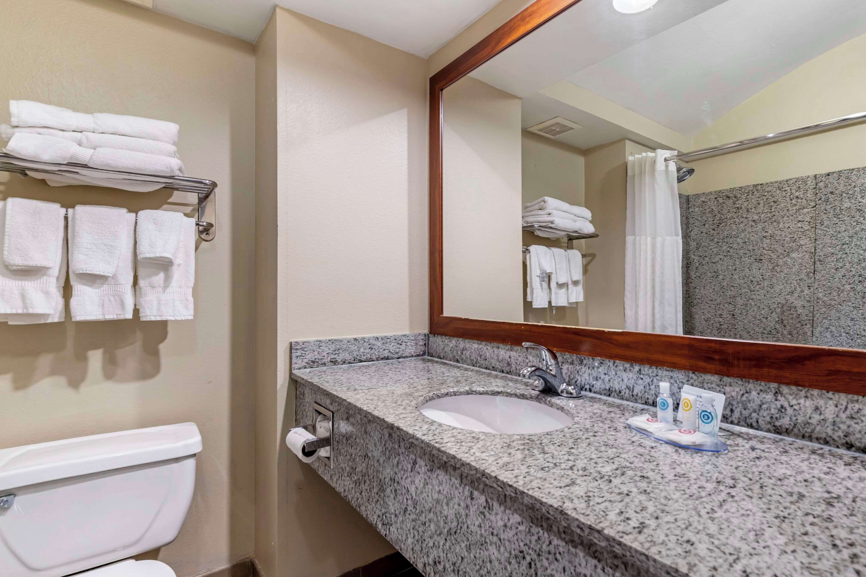 A bathroom with a granite countertop sink, a mirror, and a towel rack with folded towels.