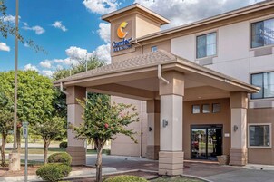 Un hotel Comfort Inn & Suites con entrada techada, cielo despejado y señal de estacionamiento.