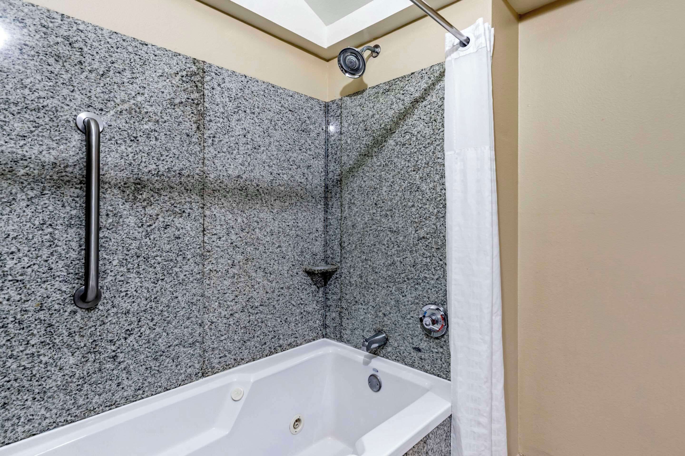Ein Badezimmer mit Duschwand aus Granit, einer weißen Badewanne und einer Handstange.