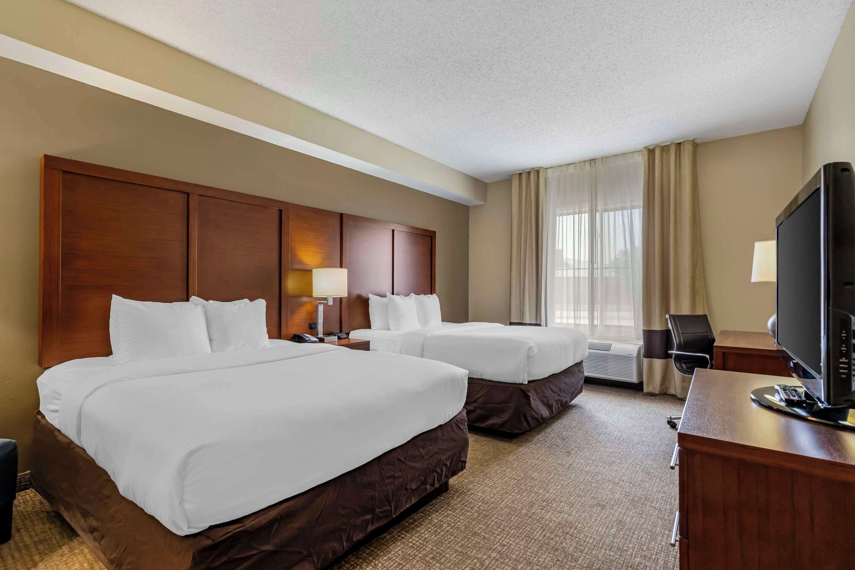 A hotel room with two beds, a desk with a television, and a window with curtains.