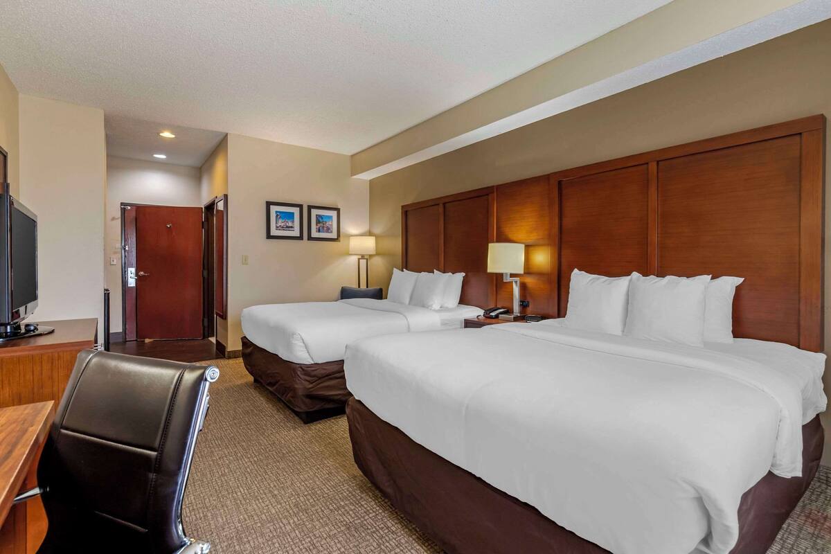 A hotel room with two beds, a desk, a chair, and a television.