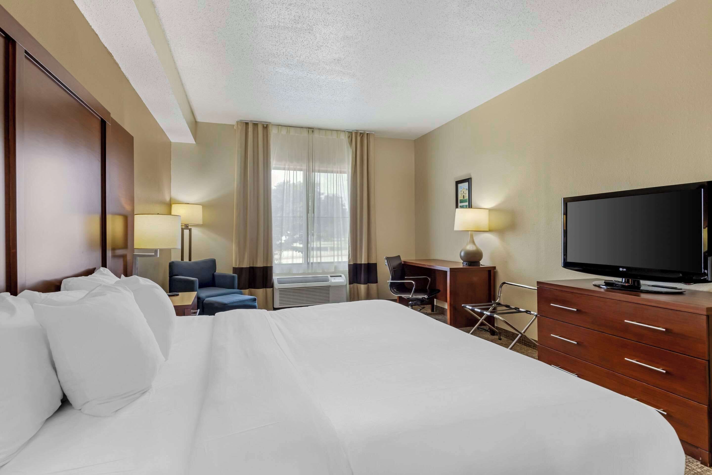 Une chambre d’hôtel avec un grand lit, un bureau, une chaise, une télévision et deux lampes.