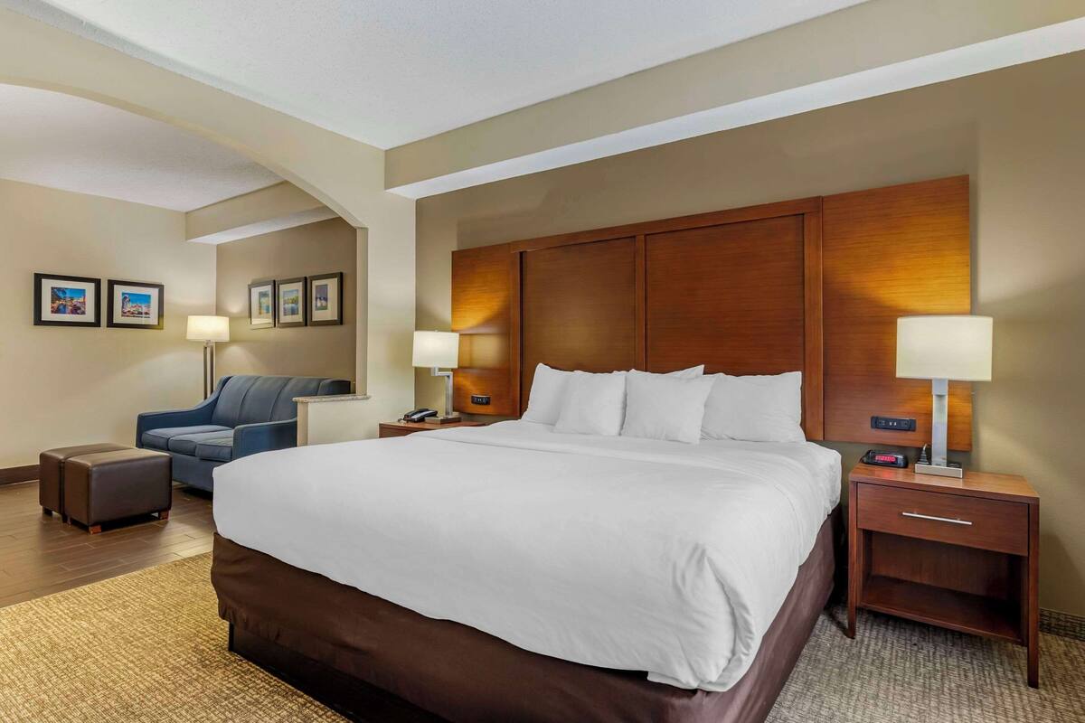 A hotel room with a large bed, two bedside tables, a desk, a chair, and a sofa.