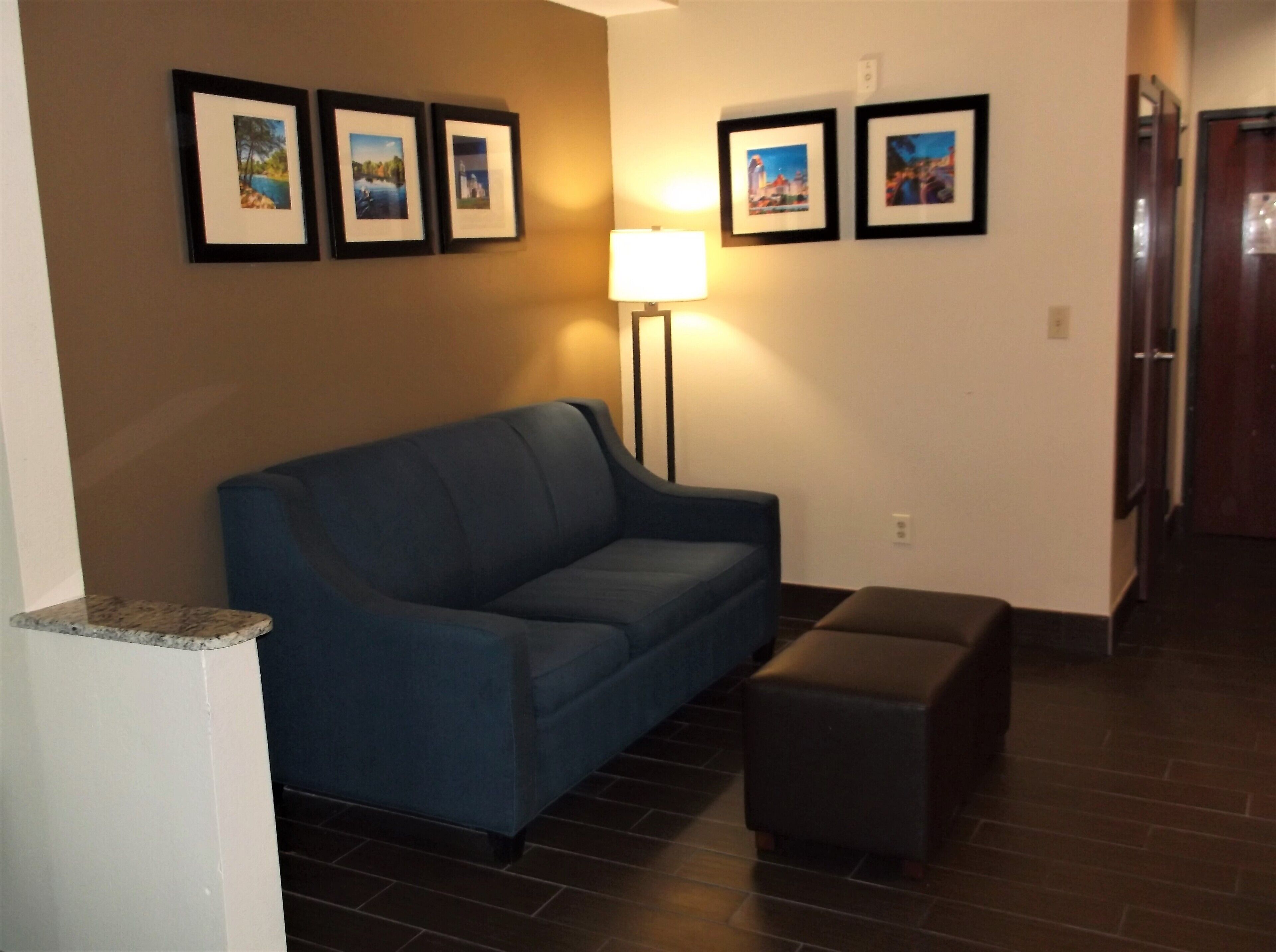 A living room with a blue sofa, a small ottoman, and a floor lamp. There are four framed pictures on the wall.