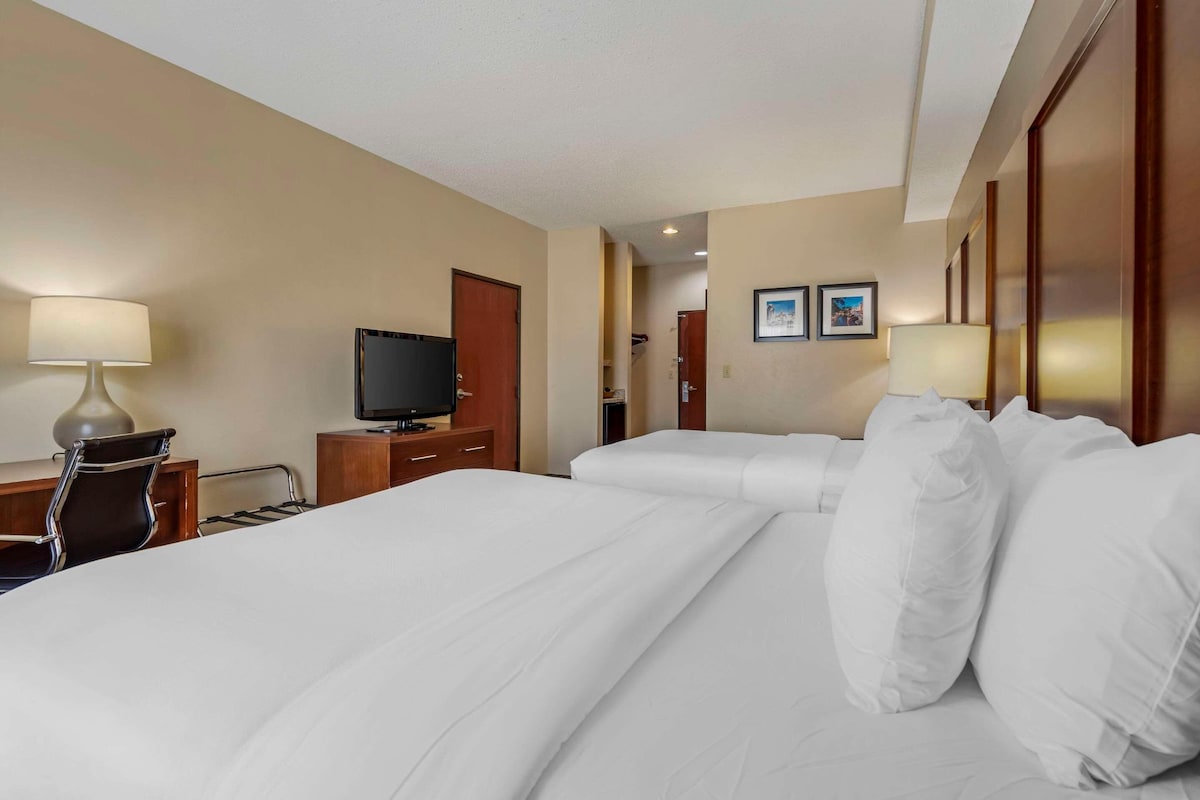A hotel room with two beds, a desk with a lamp, a television, and a door leading to a bathroom.