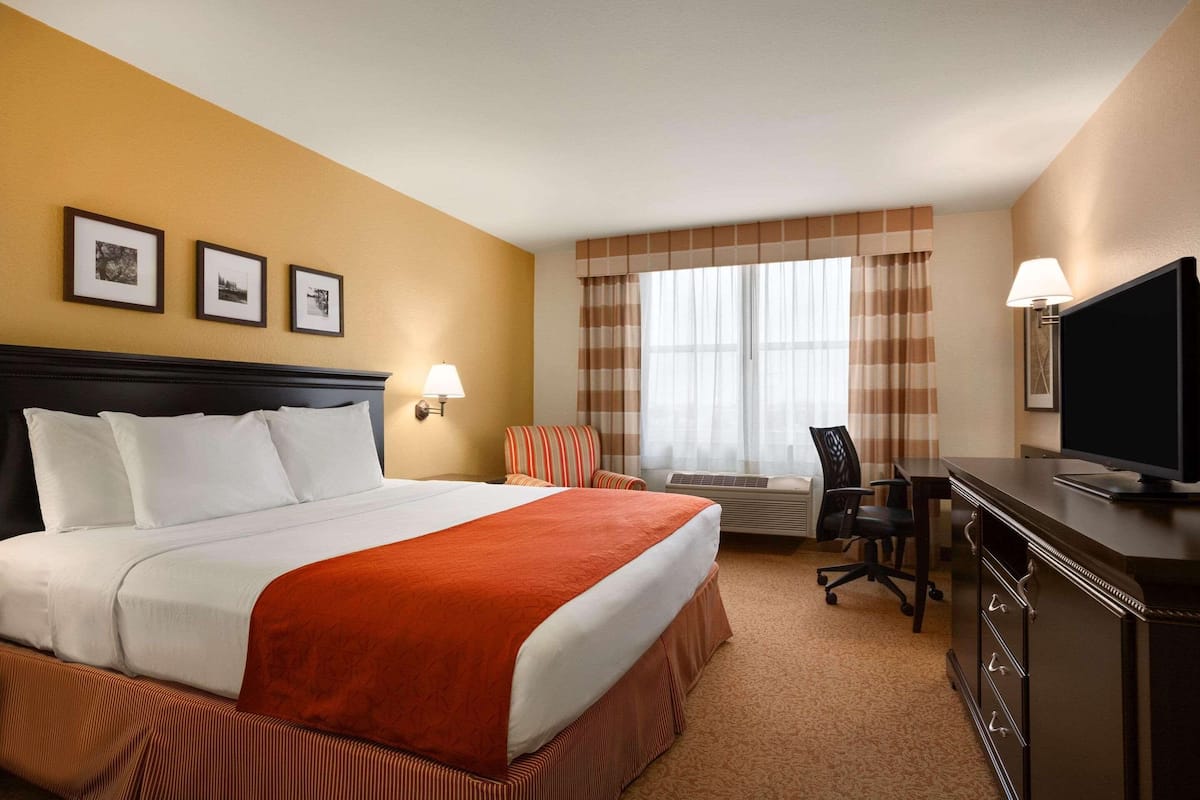 A hotel room with a large bed, a desk with a chair, a television, and a window with curtains.