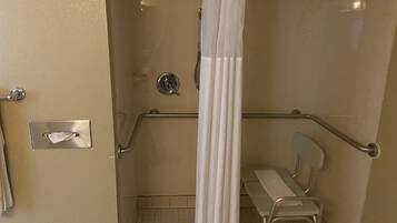 A wheelchair-accessible shower stall with a grab bar, a towel dispenser, and a bench.