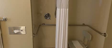 A wheelchair-accessible shower stall with a grab bar, a towel dispenser, and a bench.