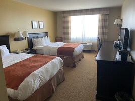 Una habitación de hotel con dos camas, un escritorio, un televisor y una ventana con cortinas.