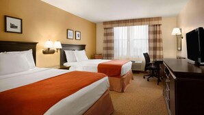 A hotel room with two beds, a desk, a chair, a television, and a window with curtains.