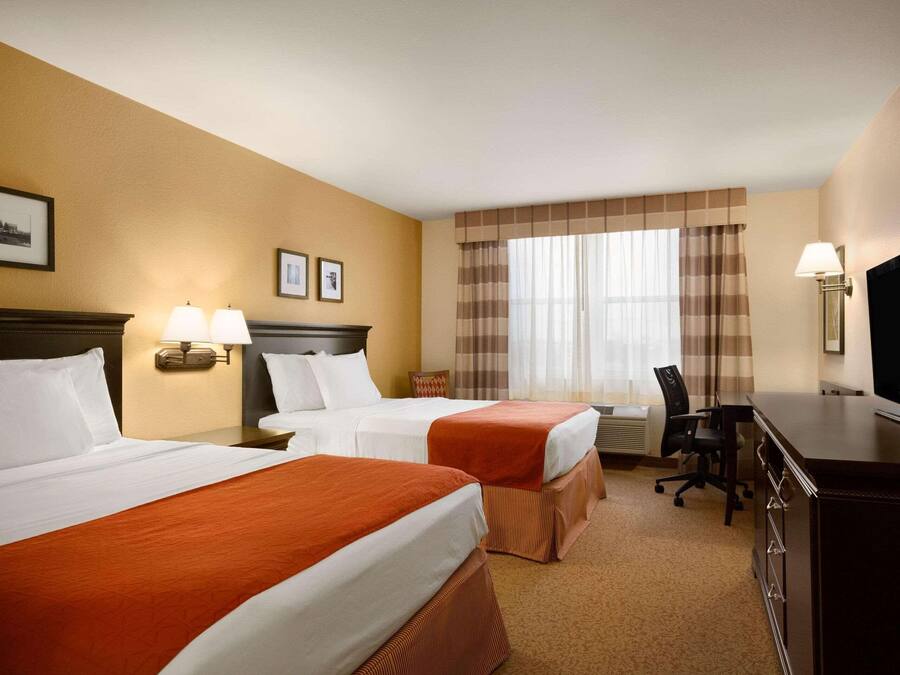 A hotel room with two beds, a desk, a chair, a television, and a window with curtains.