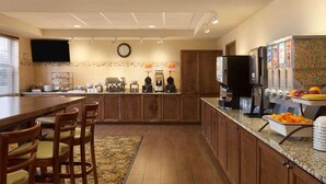 A kitchen with a wooden dining table, chairs, a clock, and a fruit display.