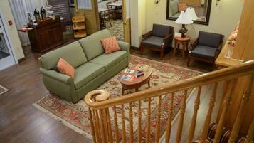 A living room with a green sofa, two armchairs, a coffee table, and a wooden staircase railing.