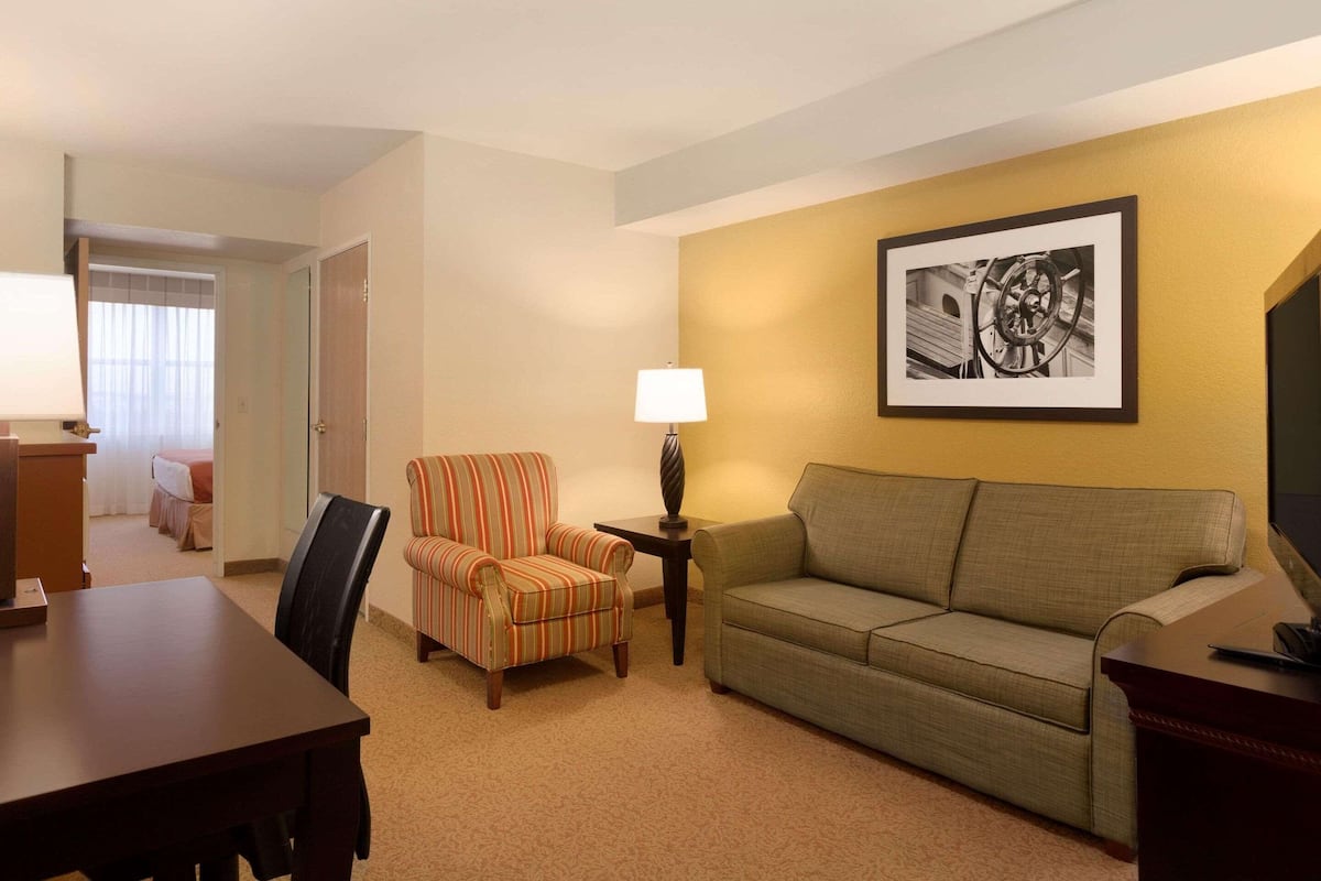 A hotel room with a dining table, striped armchair, sofa, and a lamp.