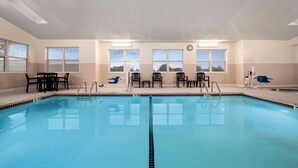 An indoor swimming pool with clear blue water, surrounded by black lounge chairs and a table.