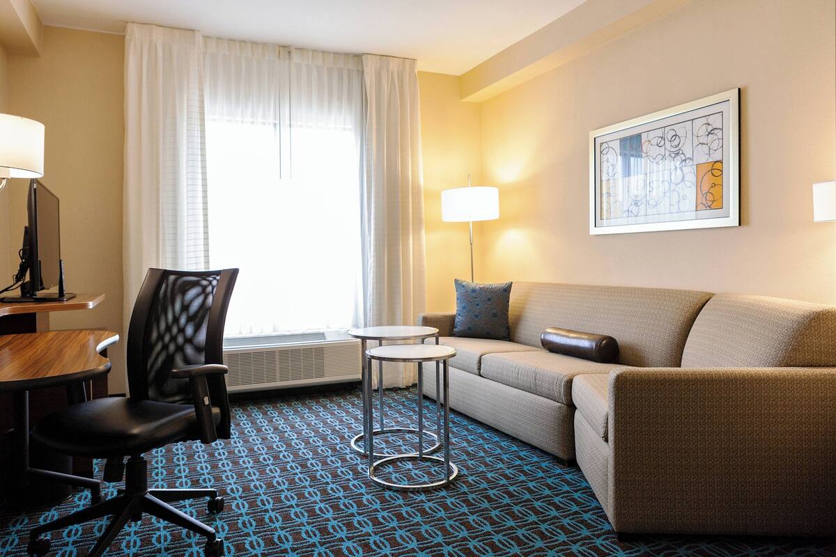 Ein Hotelzimmer mit einer Couch, einem Sessel, einem kleinen Tisch, einer Lampe und einem gerahmten Kunstwerk an der Wand.