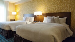 A hotel room with two beds, a wooden headboard, a nightstand with a lamp, and a patterned wall. - Fairfield Inn & Suites by Marriott Rockingham (Rockingham)