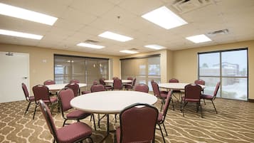 A conference room with round tables and chairs, large windows, and a carpeted floor.