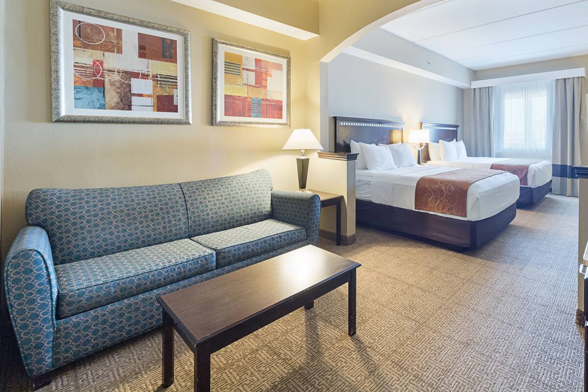 A hotel room with a sofa, a bed, a small table, and two lamps.