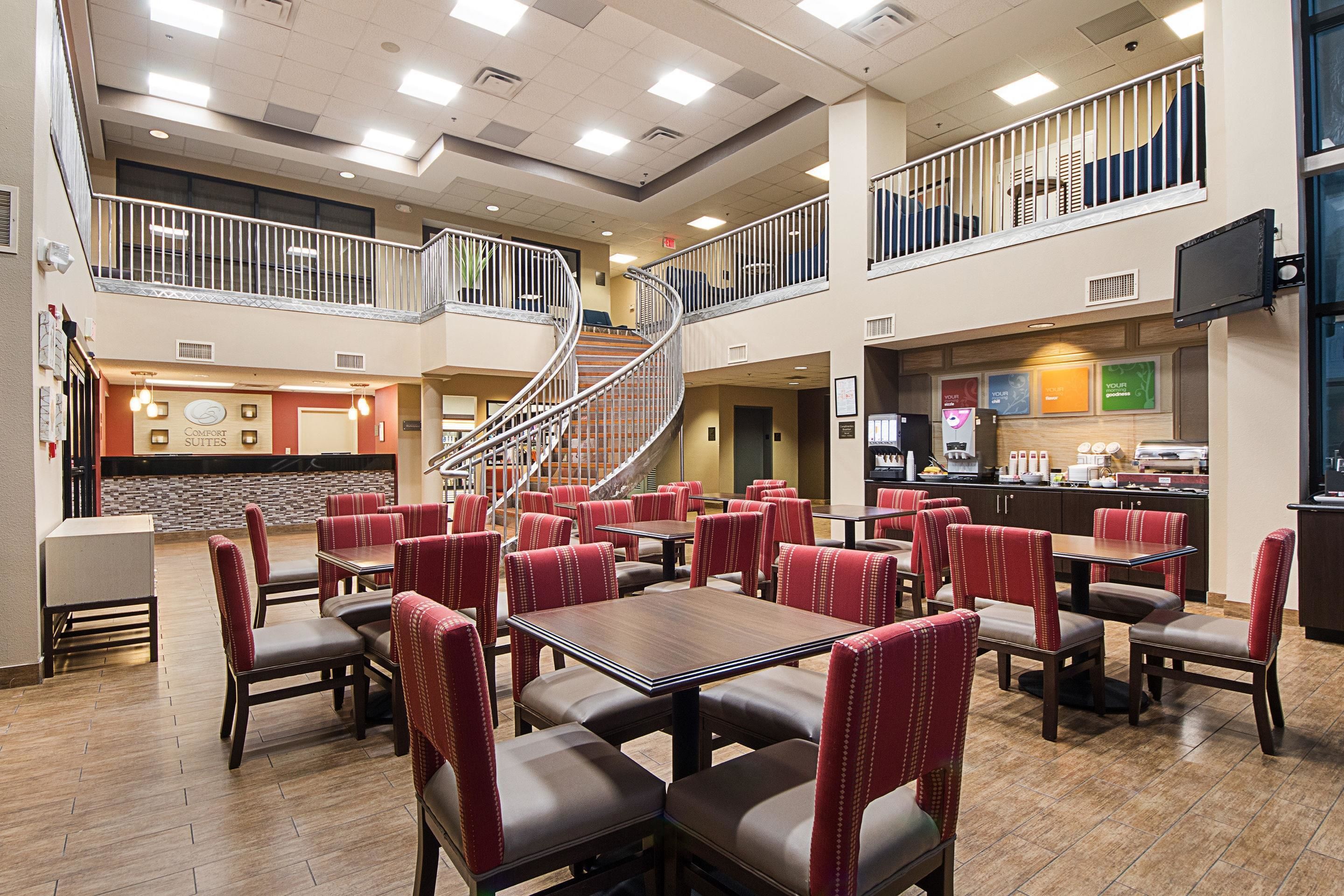 A hotel lobby with multiple dining areas, a staircase, and a kitchen area.
