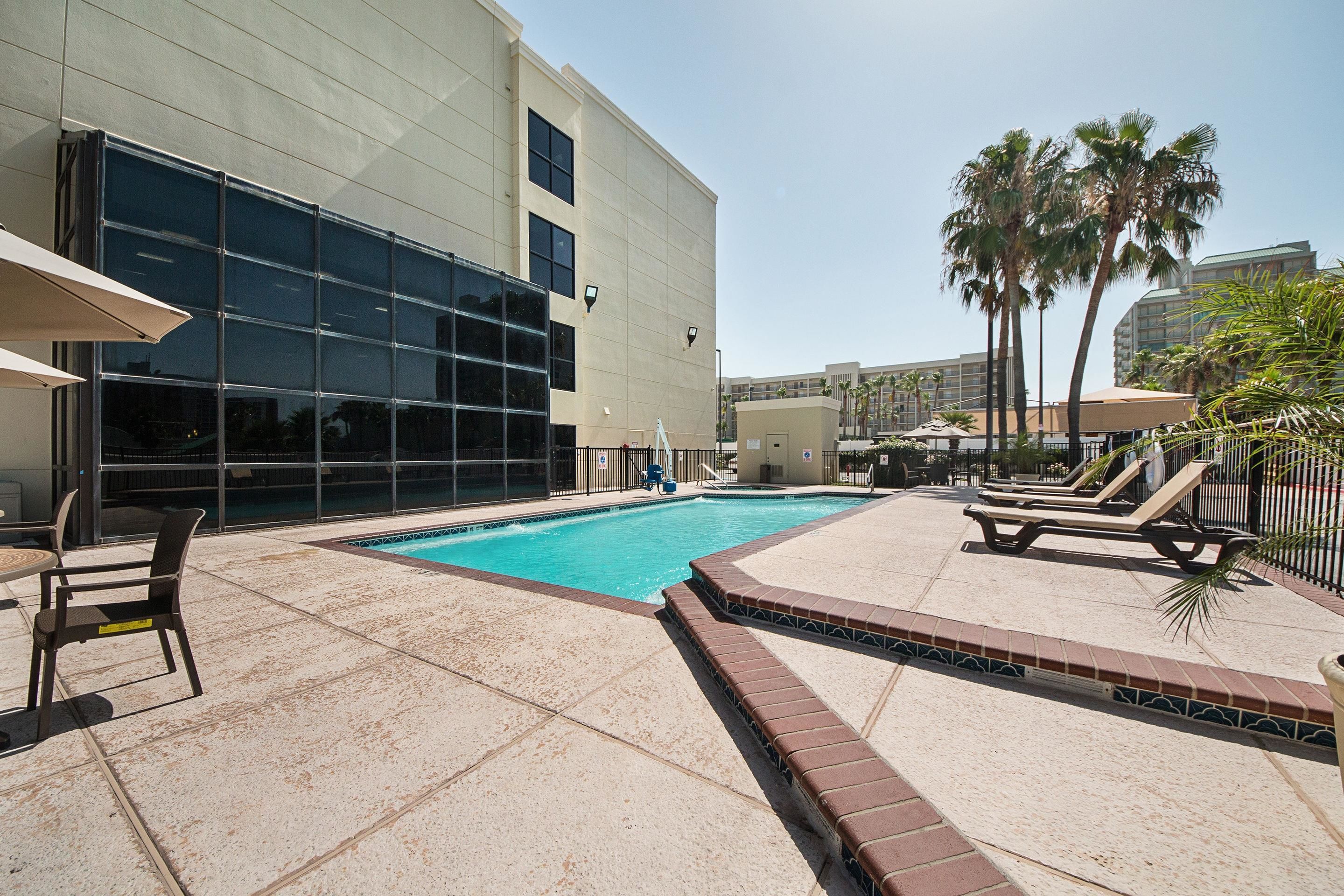 A swimming pool area with lounge chairs and a building with large windows.