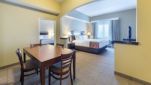 A hotel room with a wooden dining table, two chairs, a bed with a headboard, a nightstand with lamps, and a television on a stand. - Comfort Suites Beachside (South Padre Island)