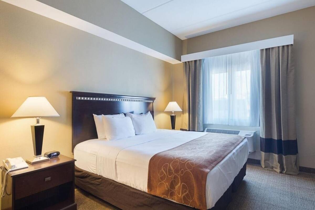 A hotel room with a large bed, two bedside lamps, a nightstand with a phone, and a window with curtains.