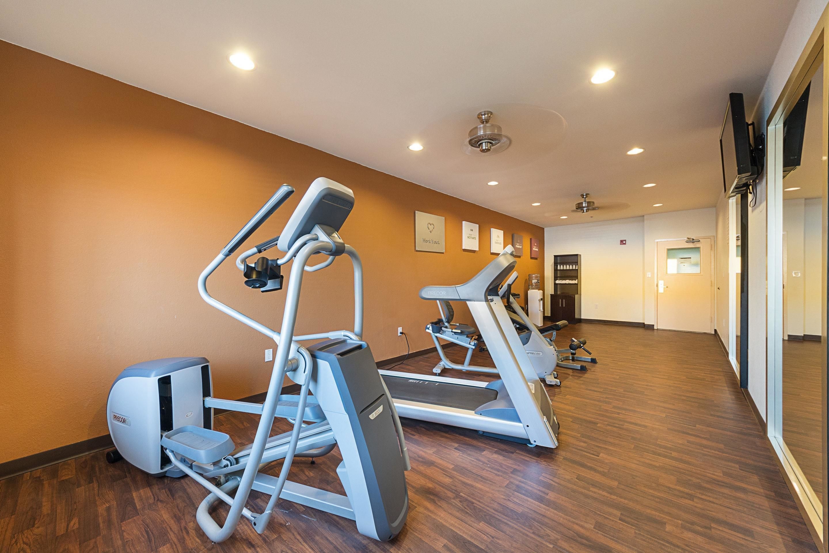 Un gimnasio con cintas de correr y máquinas elípticas, suelo de madera e iluminación empotrada en el techo.