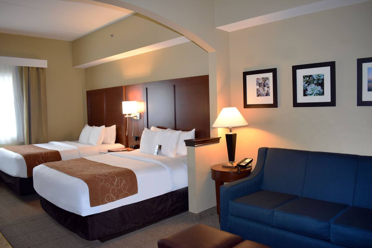 A hotel room with two beds, a blue sofa, and framed pictures on the wall.