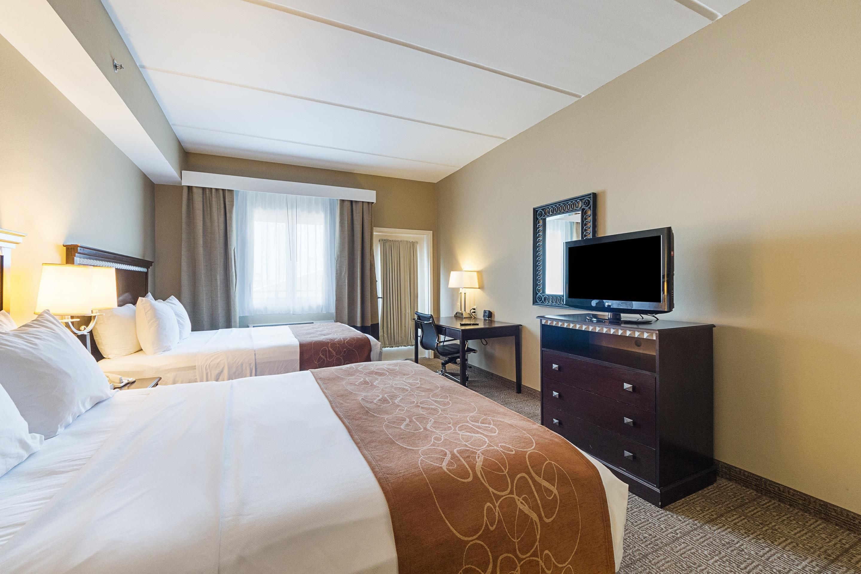 A hotel room with two beds, a desk, a television, and a dresser.