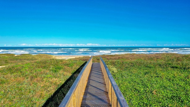A wooden boardwalk leading to a beach with ocean waves in the background. - Comfort Suites Beachside (South Padre Island)