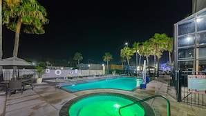 A swimming pool area with a hot tub, lounge chairs, and palm trees at night. - Comfort Suites Beachside (South Padre Island)