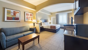 A hotel room with a sofa, a bed, a desk, and a TV. - Comfort Suites Beachside (South Padre Island)