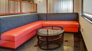A corner seating area with a round glass table, grey and orange cushioned benches, and a striped curtain backdrop. - Drury Inn & Suites Memphis Southaven (Horn Lake)