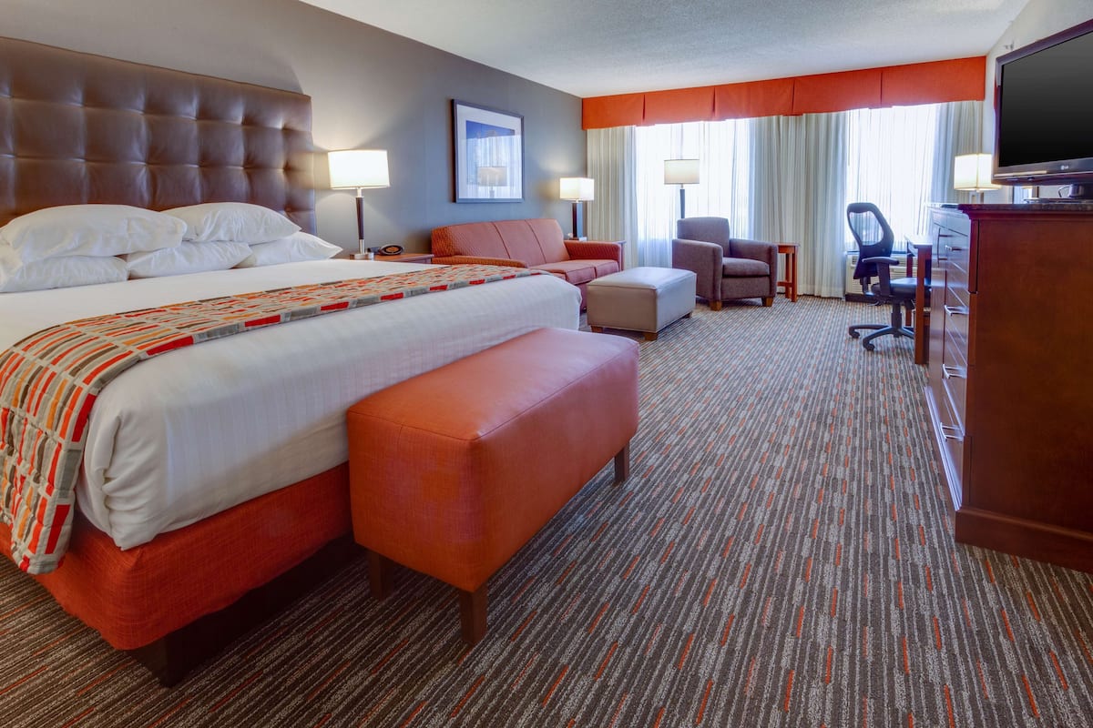 A hotel room with a large bed, a desk, a chair, and a television.