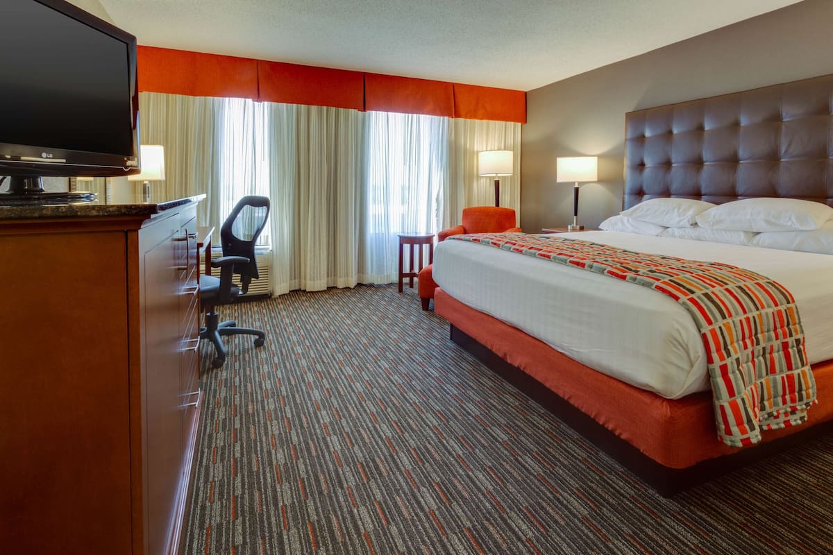 A hotel room with a large bed, a desk with a flat-screen TV, a chair, and a window with curtains.
