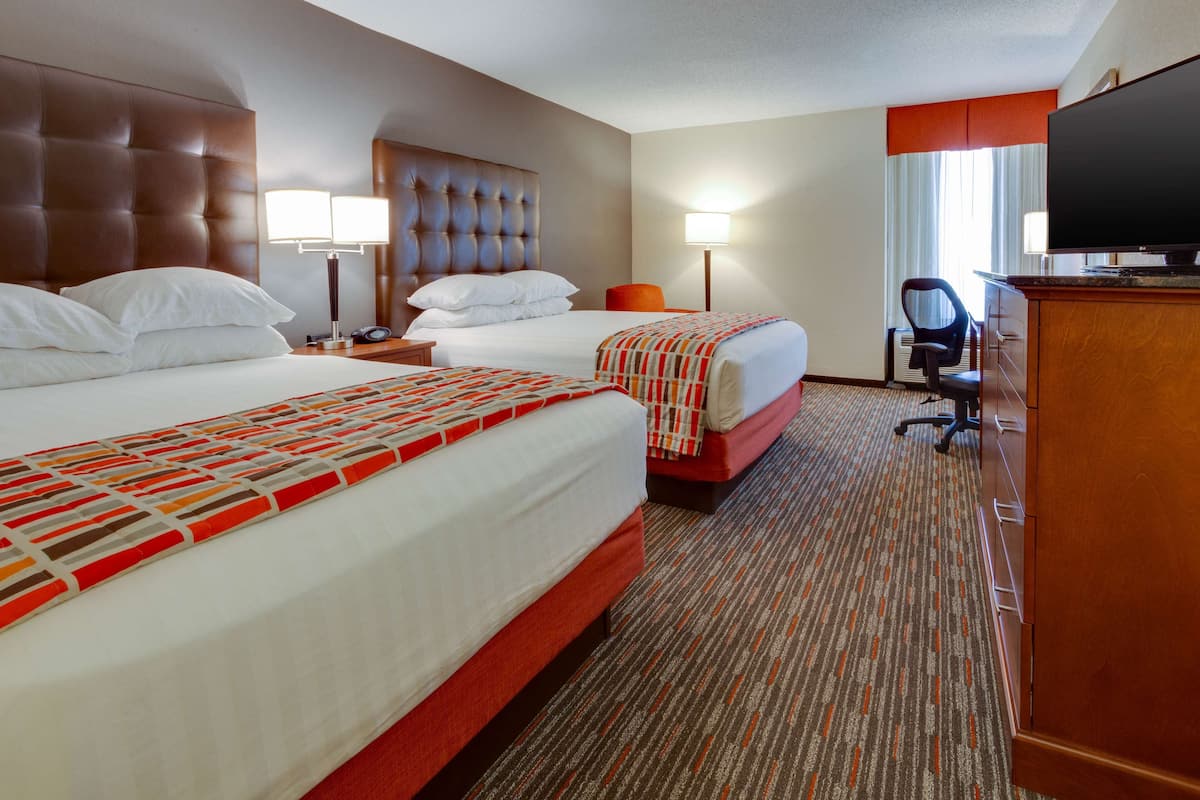 A hotel room with two beds, a television, a desk, and a chair.