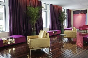A modern lounge area with purple seating, large windows, and a large plant.