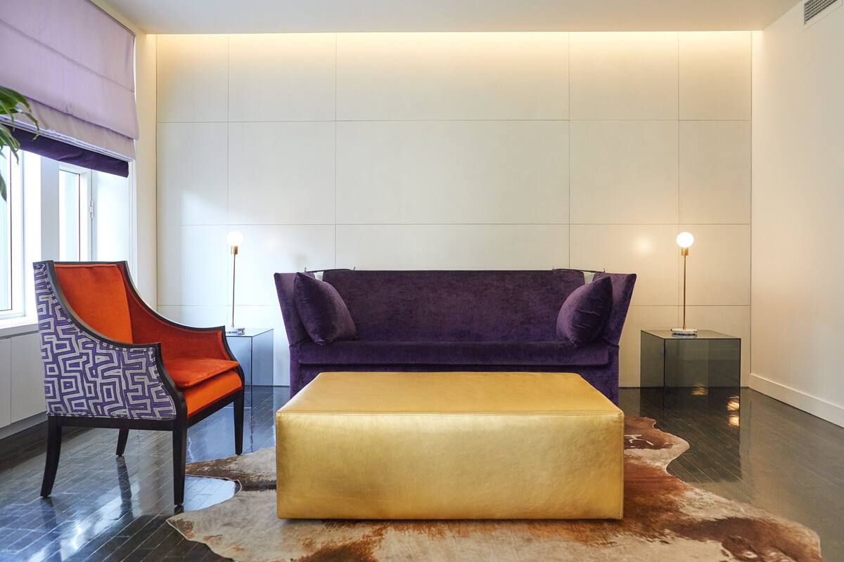A modern living room with a purple sofa, an orange chair, and a yellow ottoman on a cowhide rug.