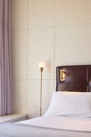 A neatly made bed with white linens, a dark headboard, and a floor lamp with a round light fixture.