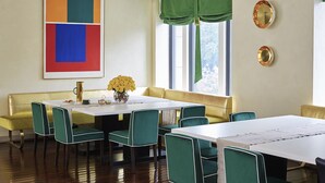 Un comedor con una mesa blanca, sillas verdes, un sofá amarillo y un cuadro abstracto grande en la pared.