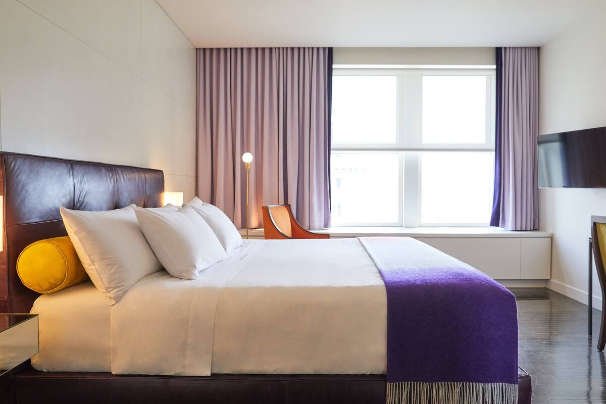 A hotel room with a large bed, a nightstand, a lamp, a chair, and a TV.