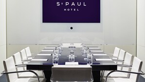 Un salón de conferencias con una larga mesa, sillas blancas y una pantalla grande que muestra "St Paul Hotel".