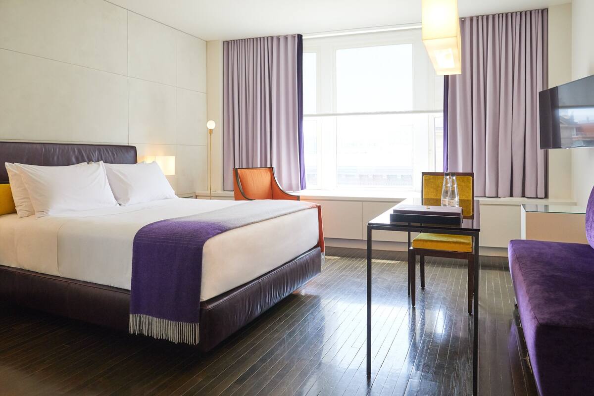 A hotel room with a large bed, a chair, a small table, and a TV.