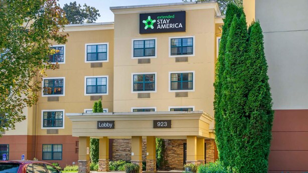 A Stay America hotel with a lobby, numbered 923, and a tall green hedge. - Extended Stay America Suites Seattle Bothell West (Bothell)