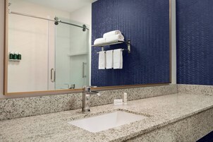 Un baño con encimera de granito, un lavamanos blanco, un espejo grande y un perchero con toallas dobladas.
