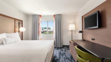 A hotel room with a bed, a desk, a television, and a window with curtains.